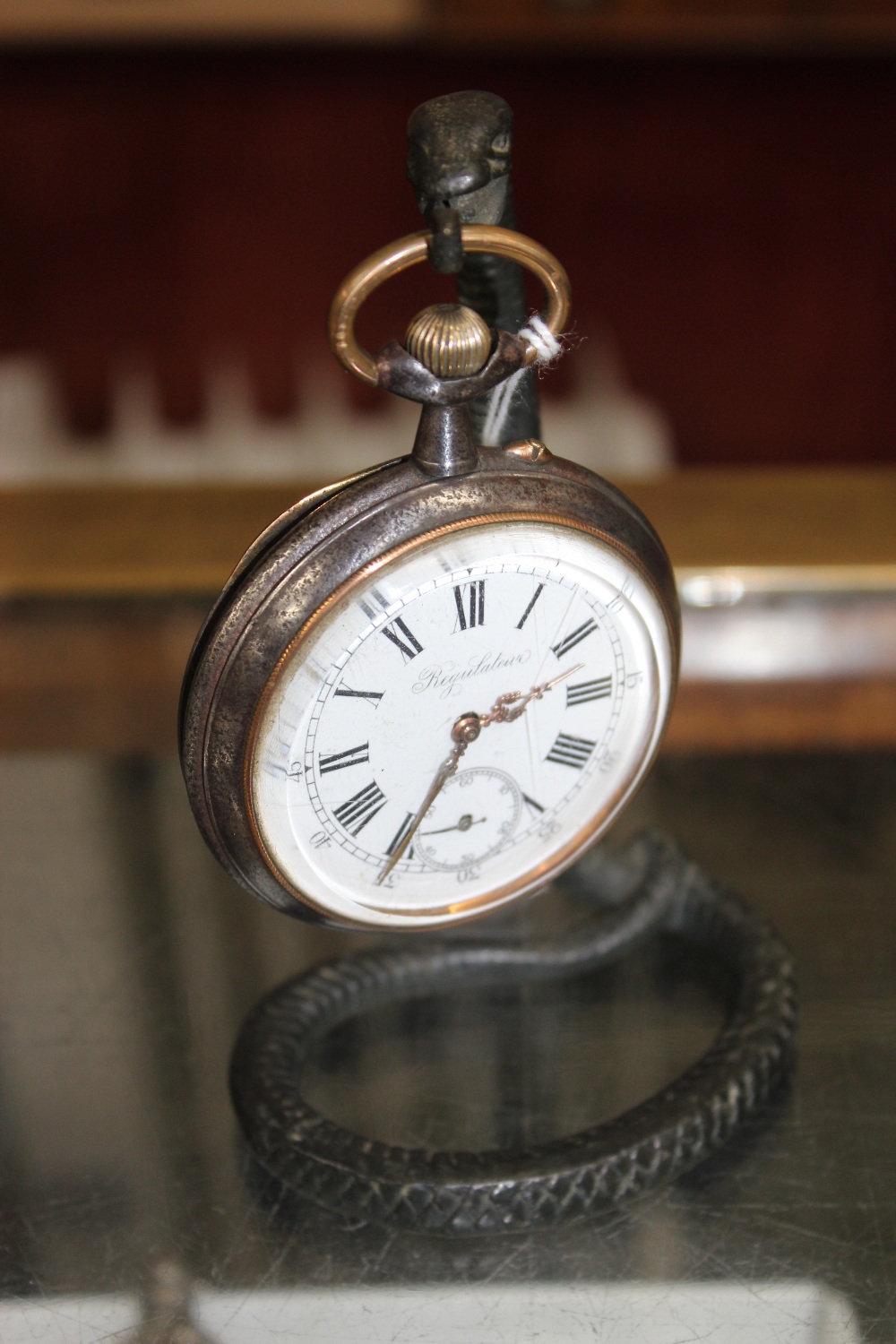 A CAST METAL WATCH STAND in the form of a snake holding an old pocket watch with steel case, the