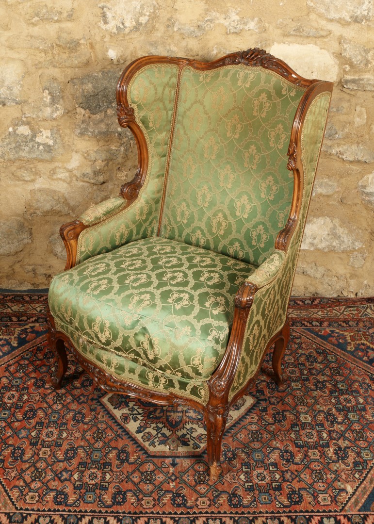 A FRENCH LOUIS XV STYLE WING ARMCHAIR with carved beech wood frame and upholstered in green ground