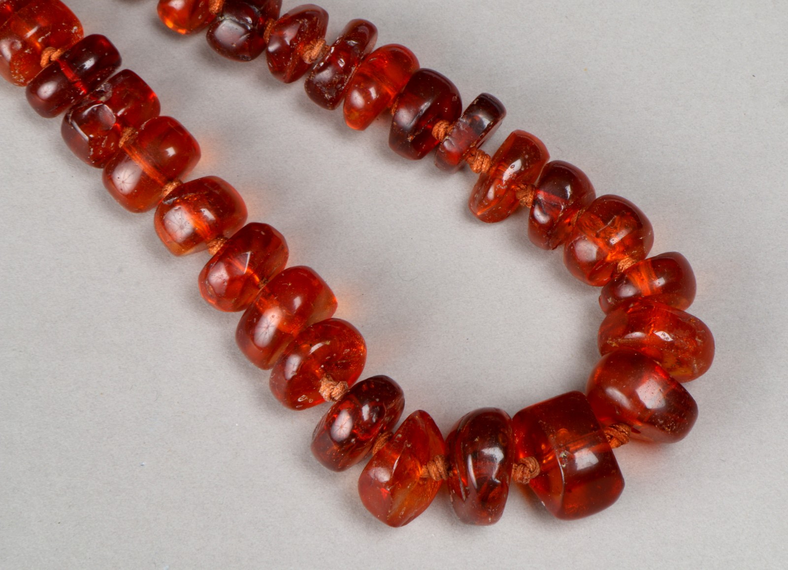 A GRADUATED AMBER BEAD NECKLACE with clear dark sherry colour irregular cut beads, 22" long, 87