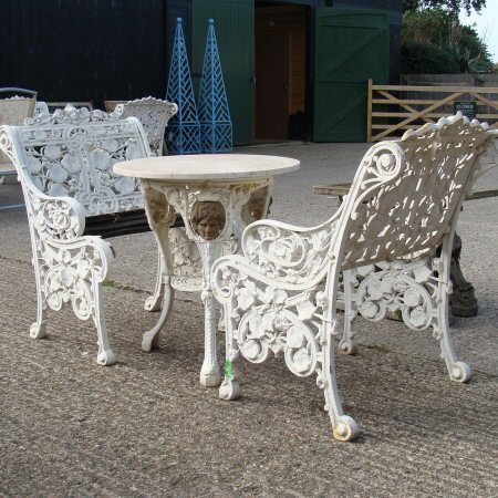 A pair of white painted cast iron garden chairs, together with a cast iron garden table, with a