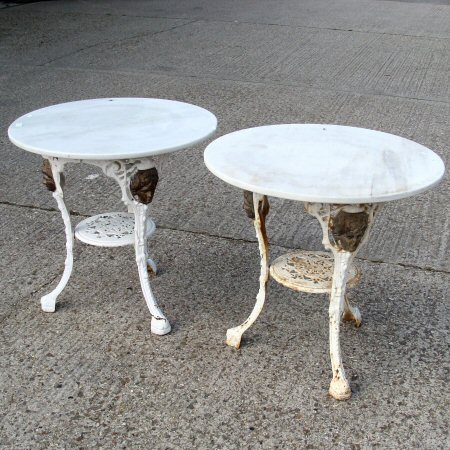 A pair of white painted cast iron garden tables, each with a circular marble top,