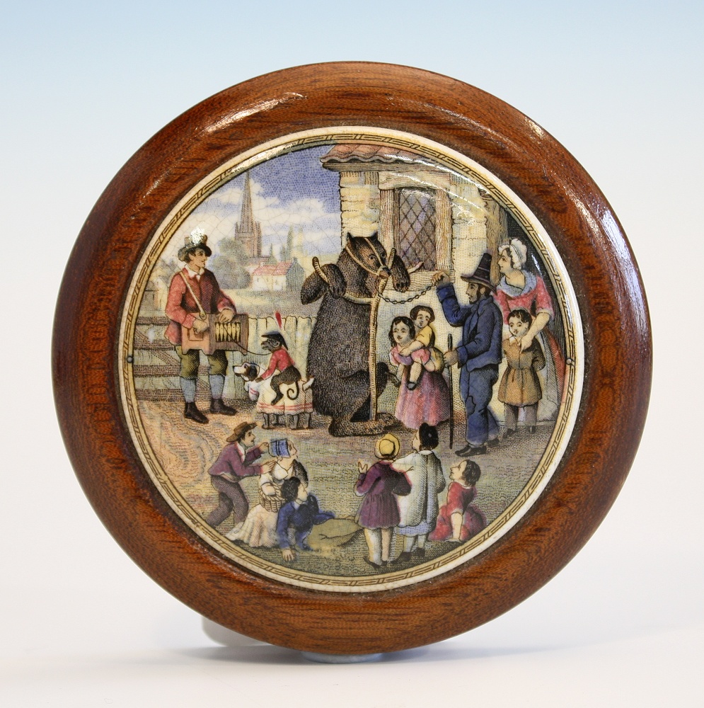 A Prattware pot lid `The Village Wakes` a wooden framed mid 19th century pot lid showing a bear