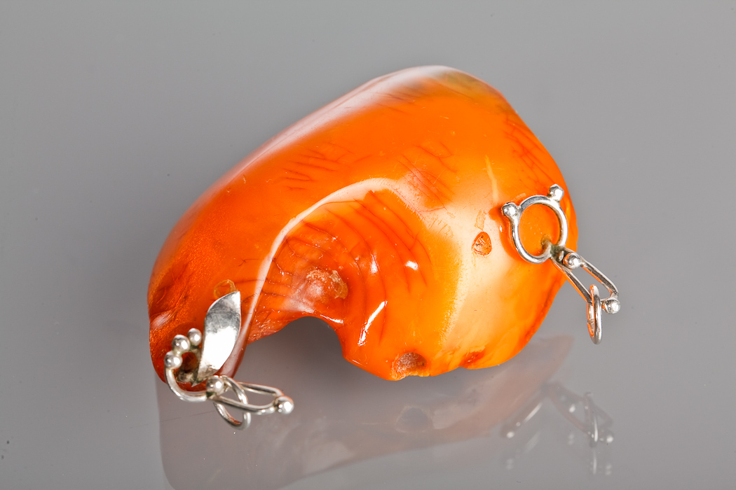 LARGE AMBER PENDANT of irregular form, approximately 65mm across, fitted with two pendant loops,