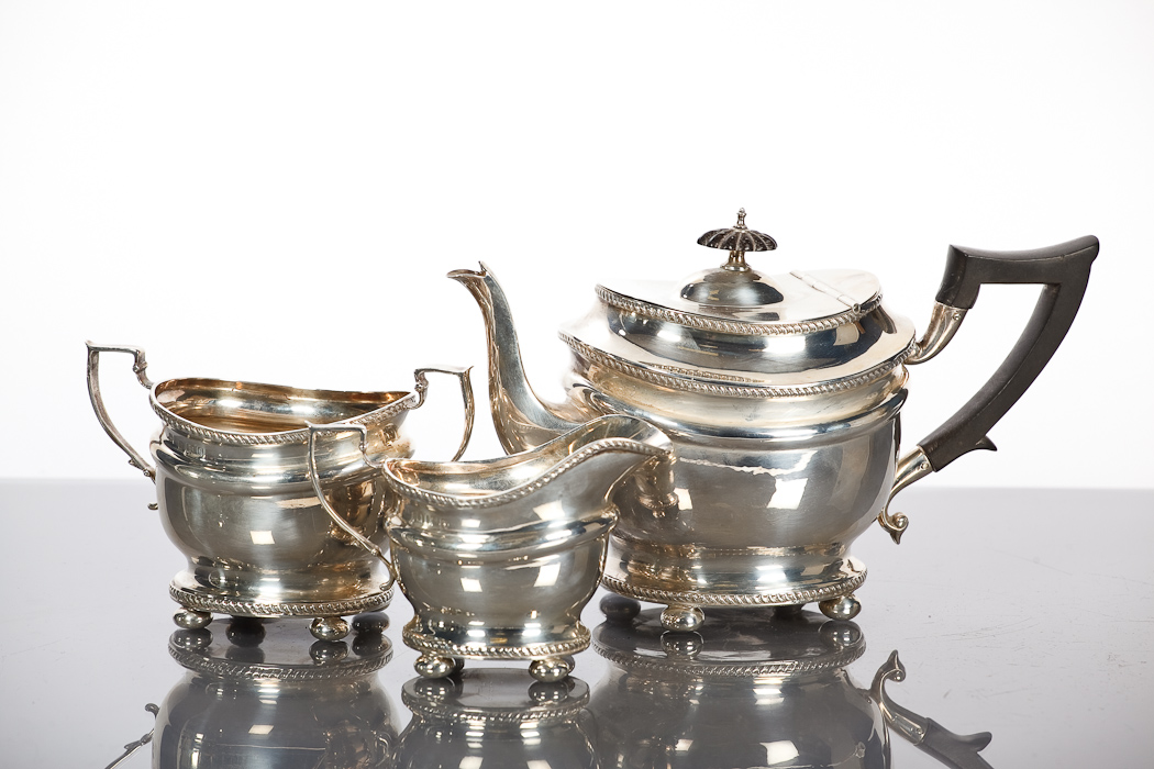 EDWARDIAN SILVER THREE PIECE TEA SERVICE of oval form, with gadrooned borders and the teapot