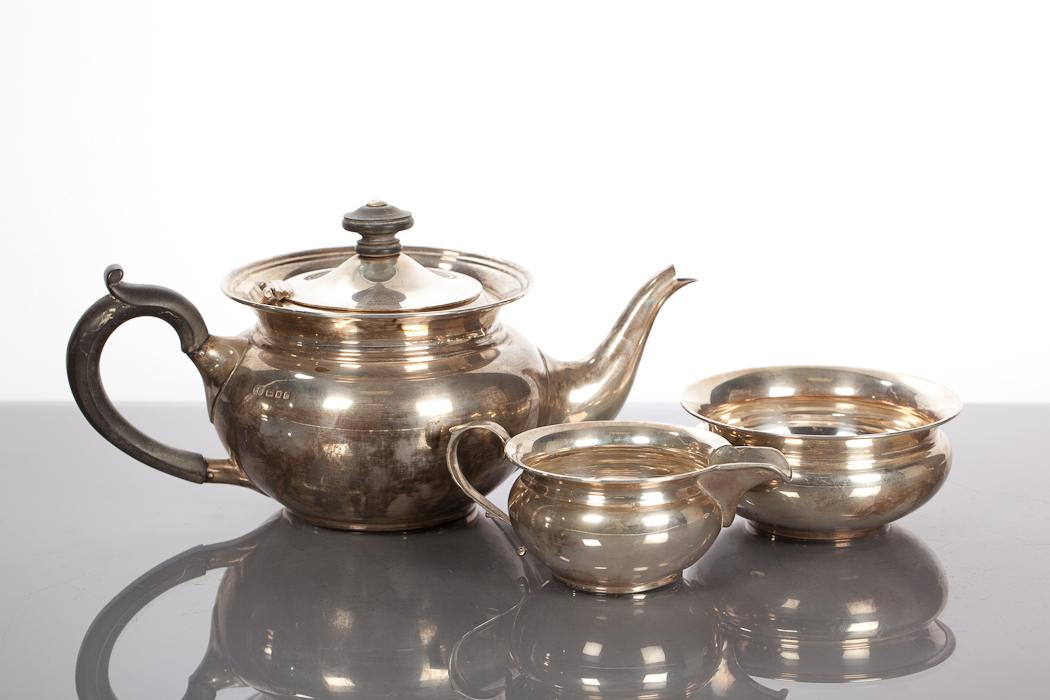 SILVER THREE PIECE TEA SERVICE each of circular form, the teapot with a hinged lid and ebonised