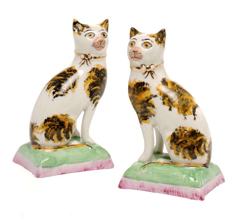 A PAIR OF STAFFORDSHIRE EARTHENWARE MODELS OF TABBY CATS seated on a green and pink fringed cushion,
