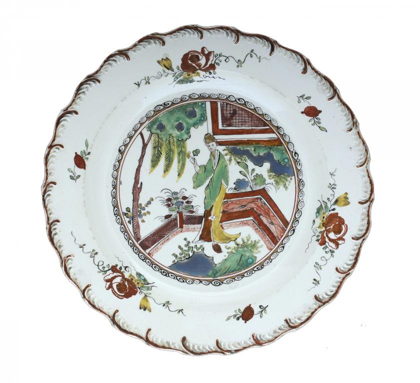 A CREAMWARE PLATE enamelled and gilt with a tall Chinese figure by a fence, in feather moulded