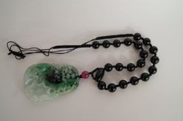 An oriental carved green and black jade pendant, carved in relief of a spider and web, on a black