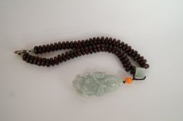 A carved green oriental jade pendant of a lotus, on a hardwood bead necklace