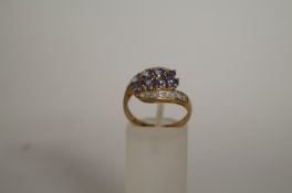 A tanzanite and diamond 9ct gold ring, the eight oval cuts to cross over shoulders set with single