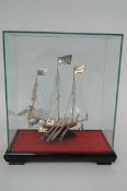 A white metal model of a Chinese junk boat in a glass case