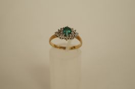 An emerald and diamond 9ct gold cluster ring, the oval cut stone flanked either side by six single