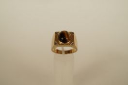 A tiger eye 9ct gold ring, the oval cabochon set to a square head, set with a small single cut