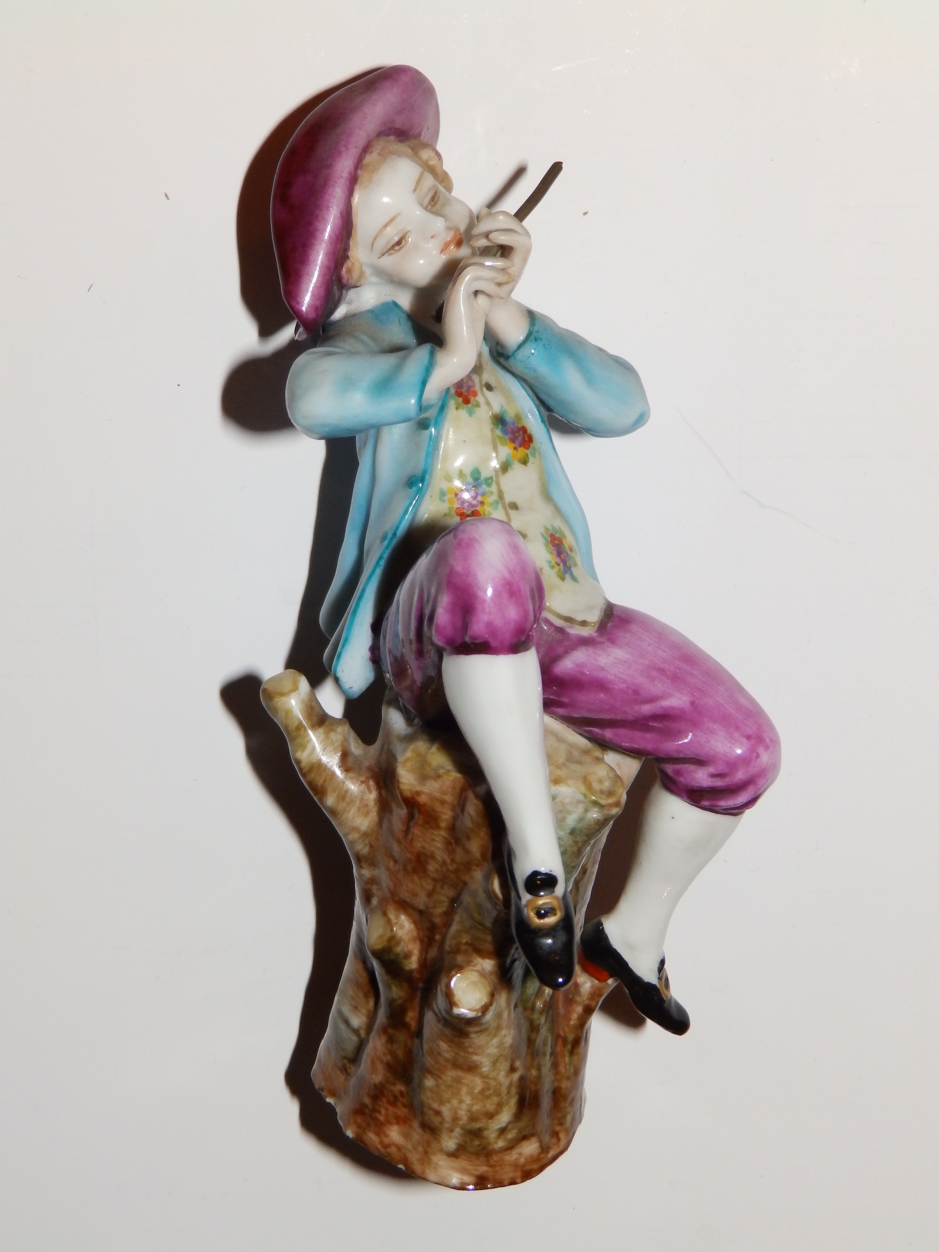 A porcelain figure of a flautist seated on a tree stump - red painted Venice anchor mark and