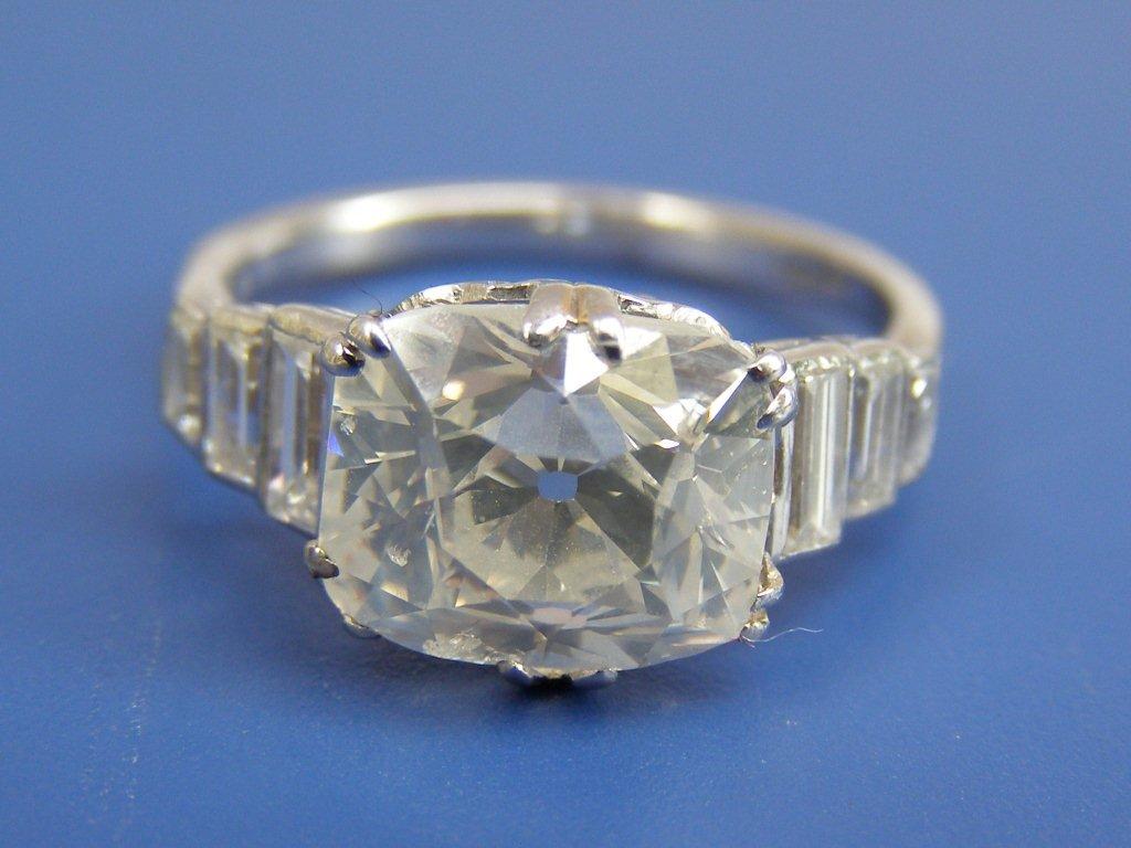 An early art deco cushion cut diamond solitaire, the claw set stone weighing 4 carats, flanked by