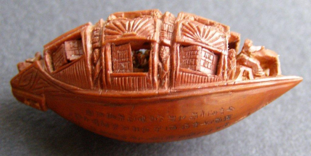 A 19thC Chinese nut carved as a crowded ship, the hull inscribed with seven lines of detailed