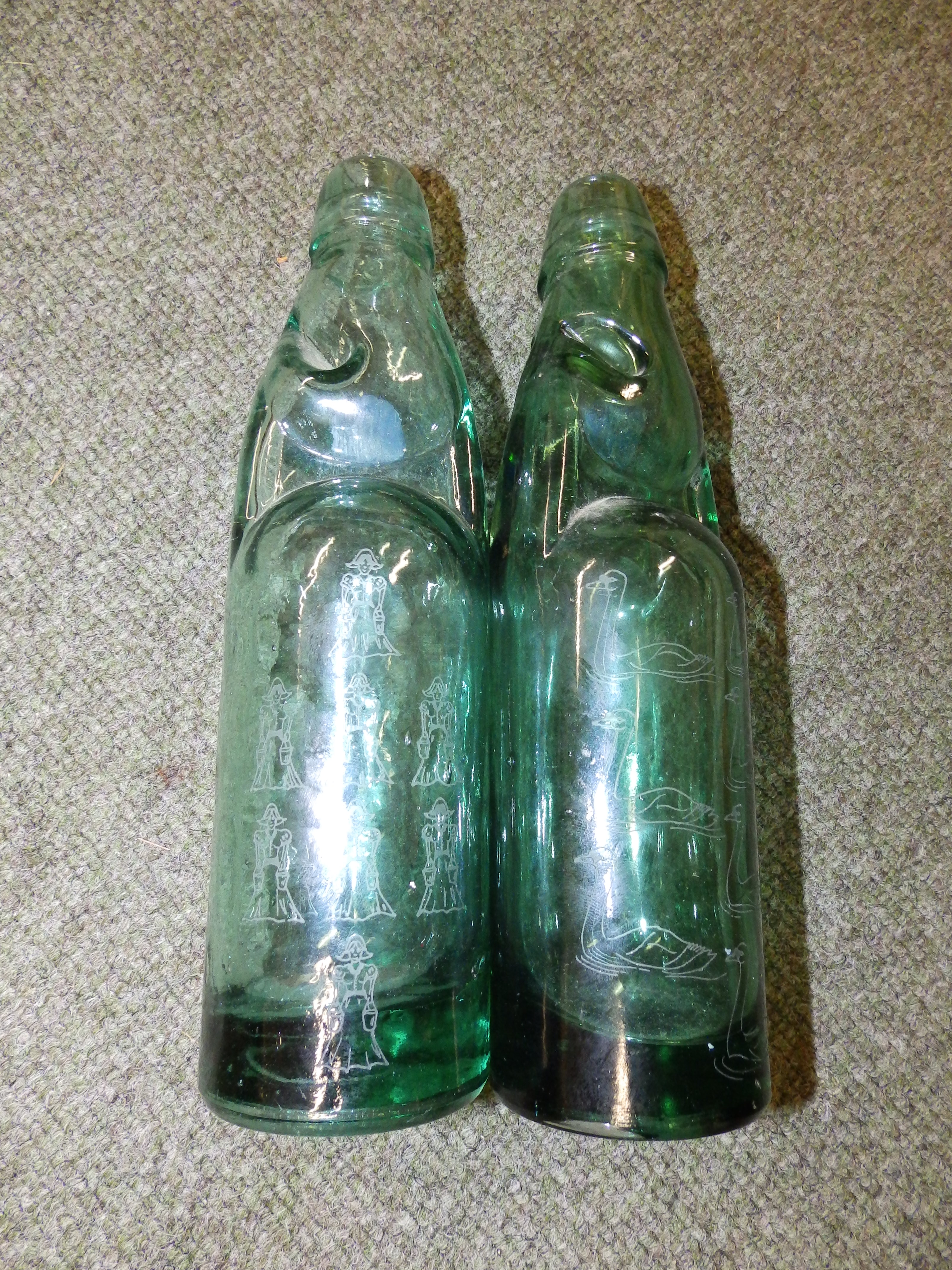 Two green glass lemonade bottles ? one engraved swans, the other milkmaids