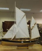 A wooden model of a sailing vessel with calico sails, raised on a wooden stand