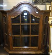 An oak corner cabinet, the shaped astragal glazed door opening to reveal two shelves