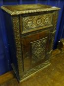 A small heavily carved oak single door cabinet with drawer to frieze, rudimentary ironwork hinges to
