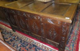 An 18th Century oak coffer, the three panelled hinged lid above a four panelled front with carved