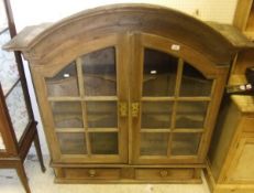 A 19th Century pine hanging cupboard, the arched cornice over two glazed doors opening to reveal