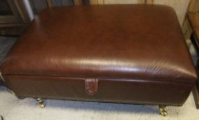A brown leather Laura Ashley footstool with lift up top compartment, on turned legs to brass