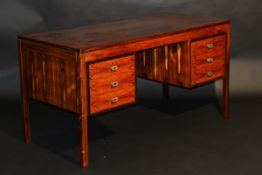 An early 1980's rosewood veneered desk, the plain top over a plain frieze and kneehole flanked by