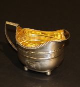 A George III silver milk jug of oval bellied form with applied reeded rim raised on four ball