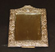 A George V silver framed easel back mirror with C scroll, bird and foliate decoration with ribbon