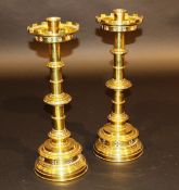 A pair of turned brass altar candlesticks in the Gothic Revival taste with castellated drip trays on