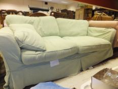 A large modern sofa with pale green loose covers and two matching scatter cushions