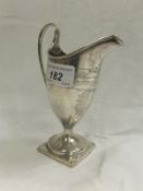 A George III silver helmet shaped cream jug with engraved cartouche bearing initials, on a square