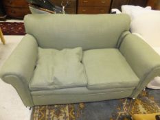 A two seat sofa raised on bun feet to castors, upholstered in green fabric