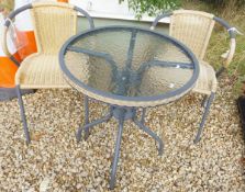 A modern metal framed circular garden table with glass top and faux wicker banding, together with