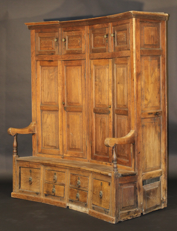 A 19th Century oak bacon settle of curved form, the upper section with moulded cornice above four