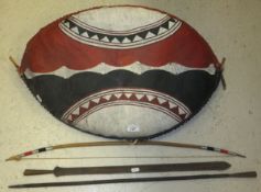 A tribal style shield decorated in red, black and white, a bow and two metal spearheads of tribal