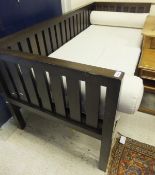 A modern oak day bed with slatted back and sides and with off-white mattress and bolster cushions