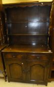 A dark stained elm dresser with three open shelves on a base of two drawers and two cupboard doors
