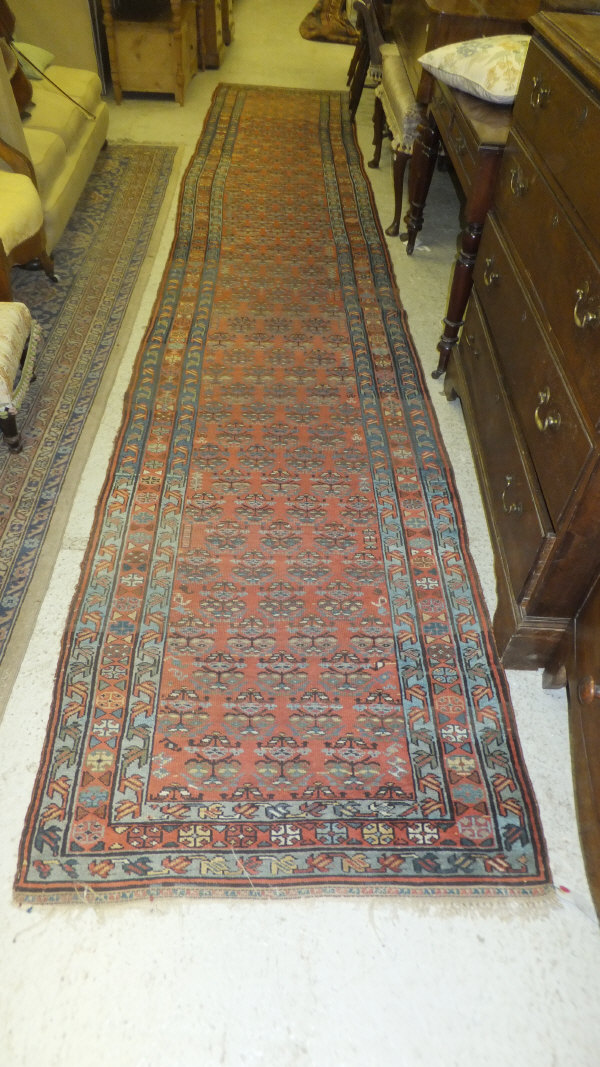 A fine Malaya runner, the central panel set with repeating stylised floral motifs on a red ground
