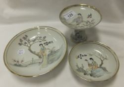 A Chinese porcelain trio, each piece painted with a lady in traditional dress, beside a blossoming
