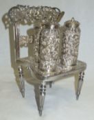 An Indian white metal three piece cruet on a base in the form of a chair, with all over heavy