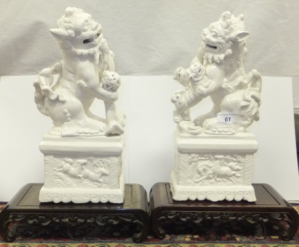 A pair of Chinese blanc-de-chine porcelain fo dog ornaments, each on a carved wood stand   CONDITION