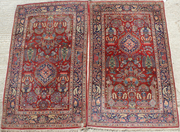 A pair of fine Kashan rugs, the central panel set with floral sprays on a red ground within a