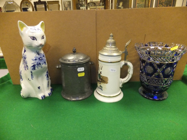 A pottery beer stein, a ceramic cat ornament, a cut glass vase with blue overlay and a hammered