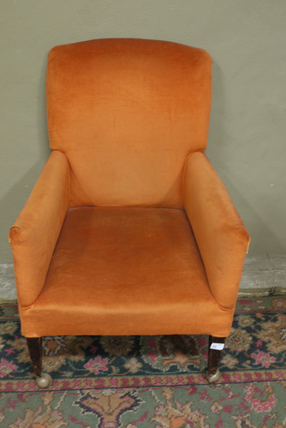 An Edwardian armchair, upholstered in burnt orange and on square tapered legs with later castors
