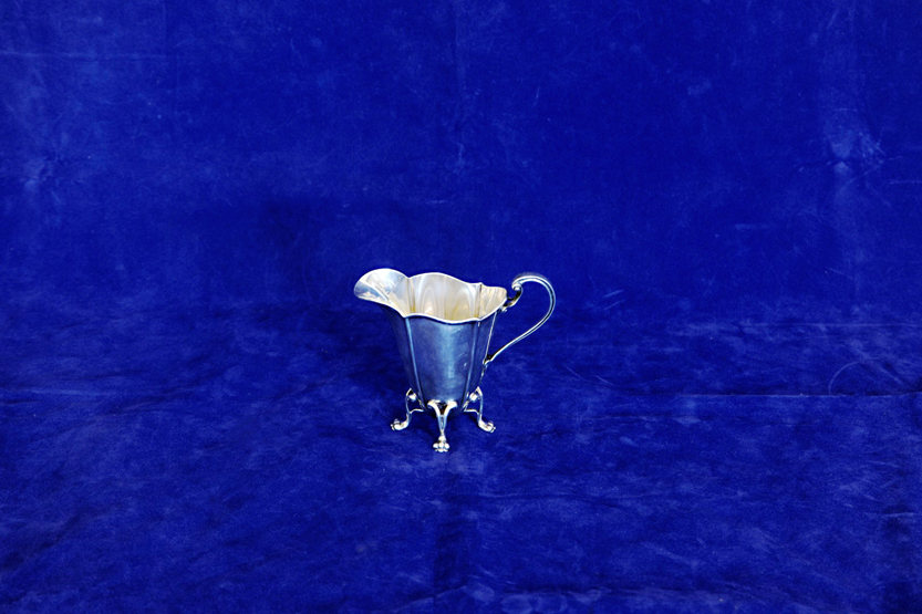 An Edward VII silver cream jug with scrolled handle and tapering body raised on four stylised pad