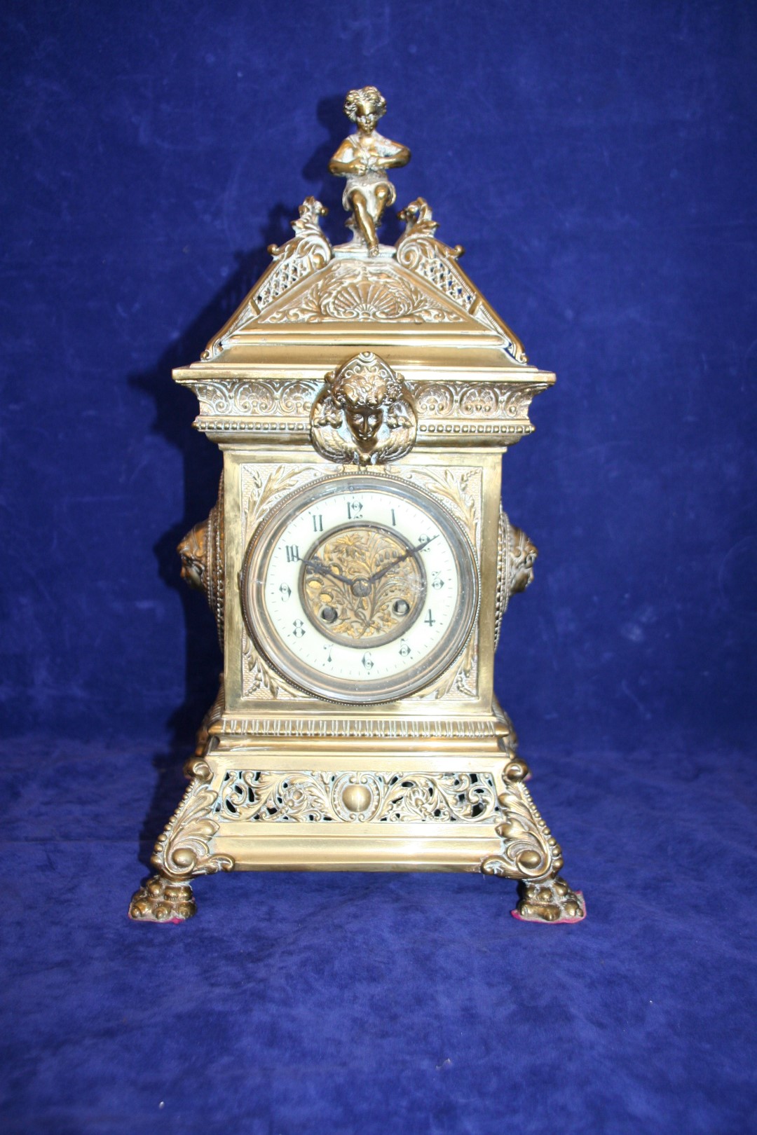 A 19th century brass cased eight day mantel clock with figural finial, mask decoration, the