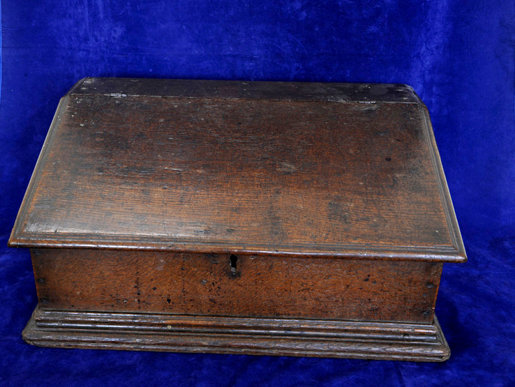 An 18th century oak bible box with sloping lid opening to reveal pigeonholed interior, on a plinth
