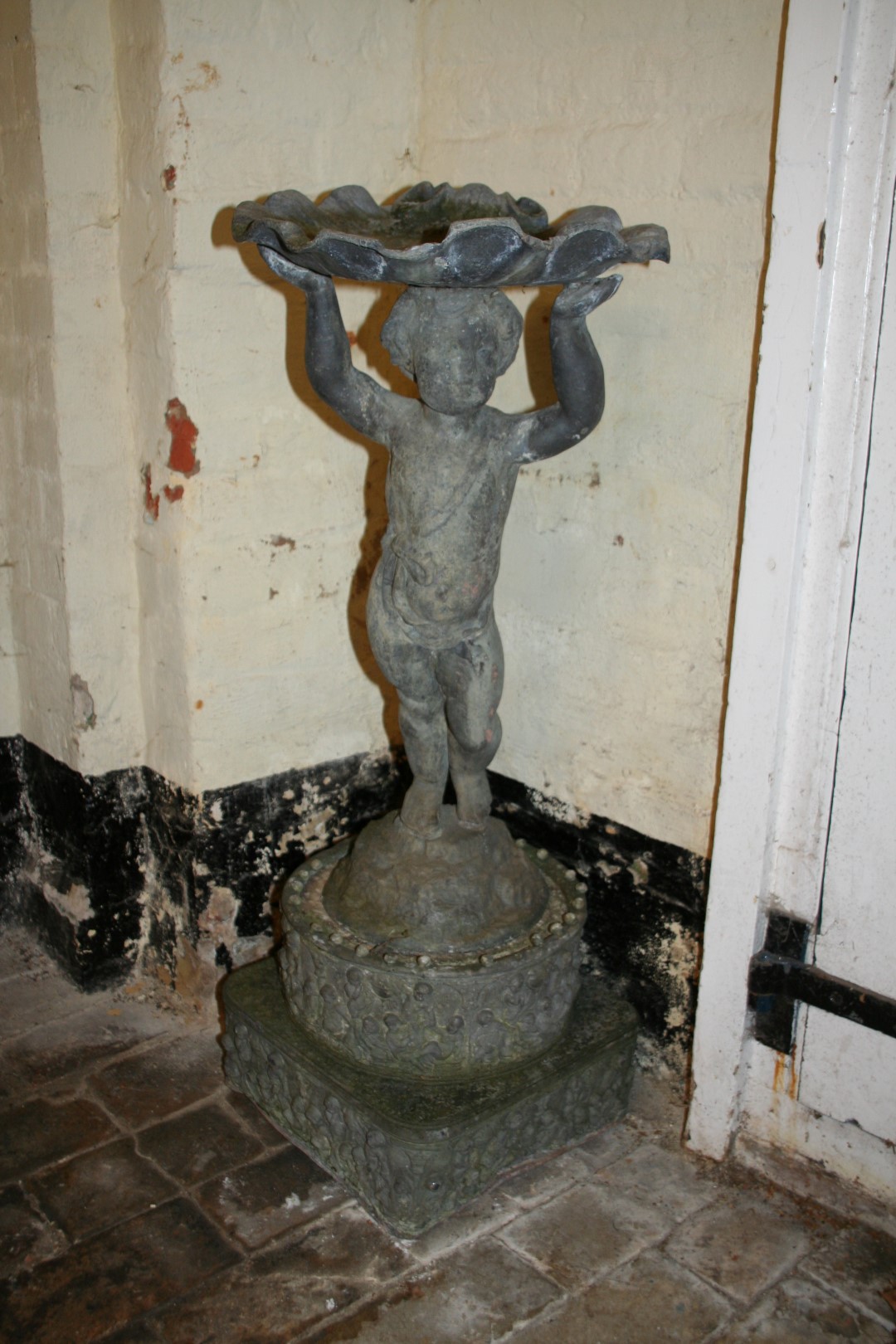 A lead bird bath with shell form top section supported by a putti with arms outstretched, on a